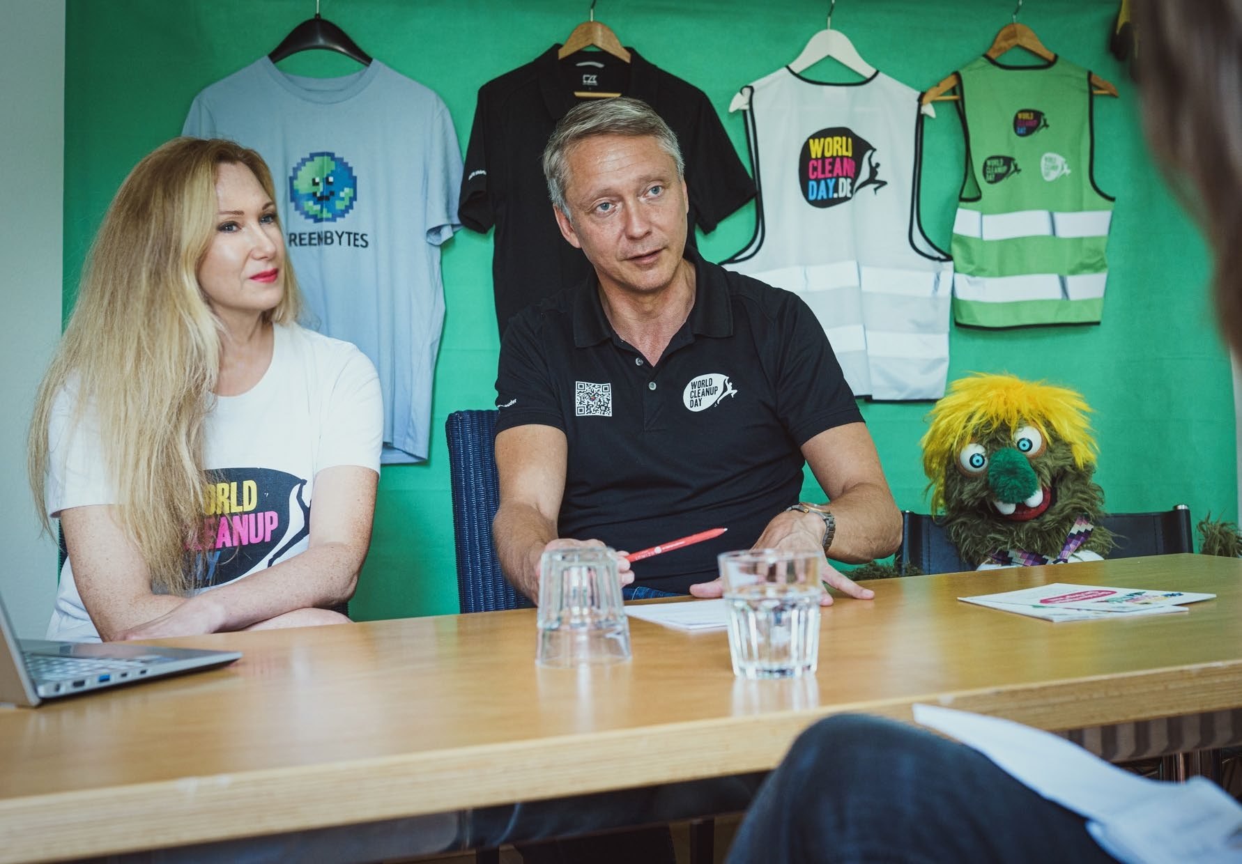 Daniela Schwerdt, Holger Holland and Olfi at a table in front of World Cleanup Day shirts and vests