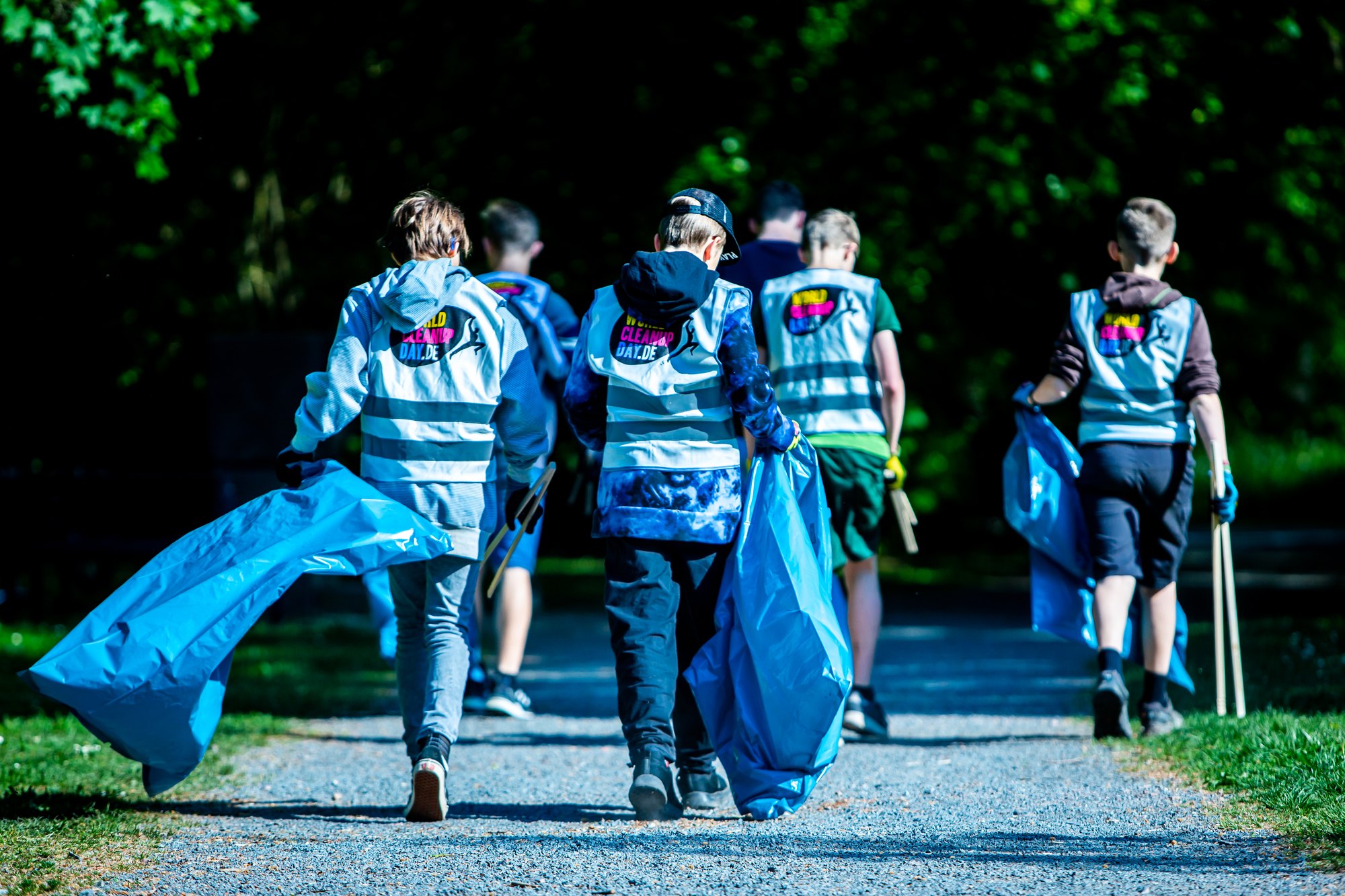 Pupils in World Cleanup Day vests carrying waste bags along a park path